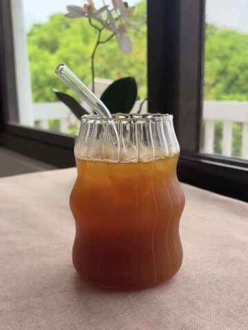 Clear straw angled down into ice-cold pineapple tea in a sculpted glass.