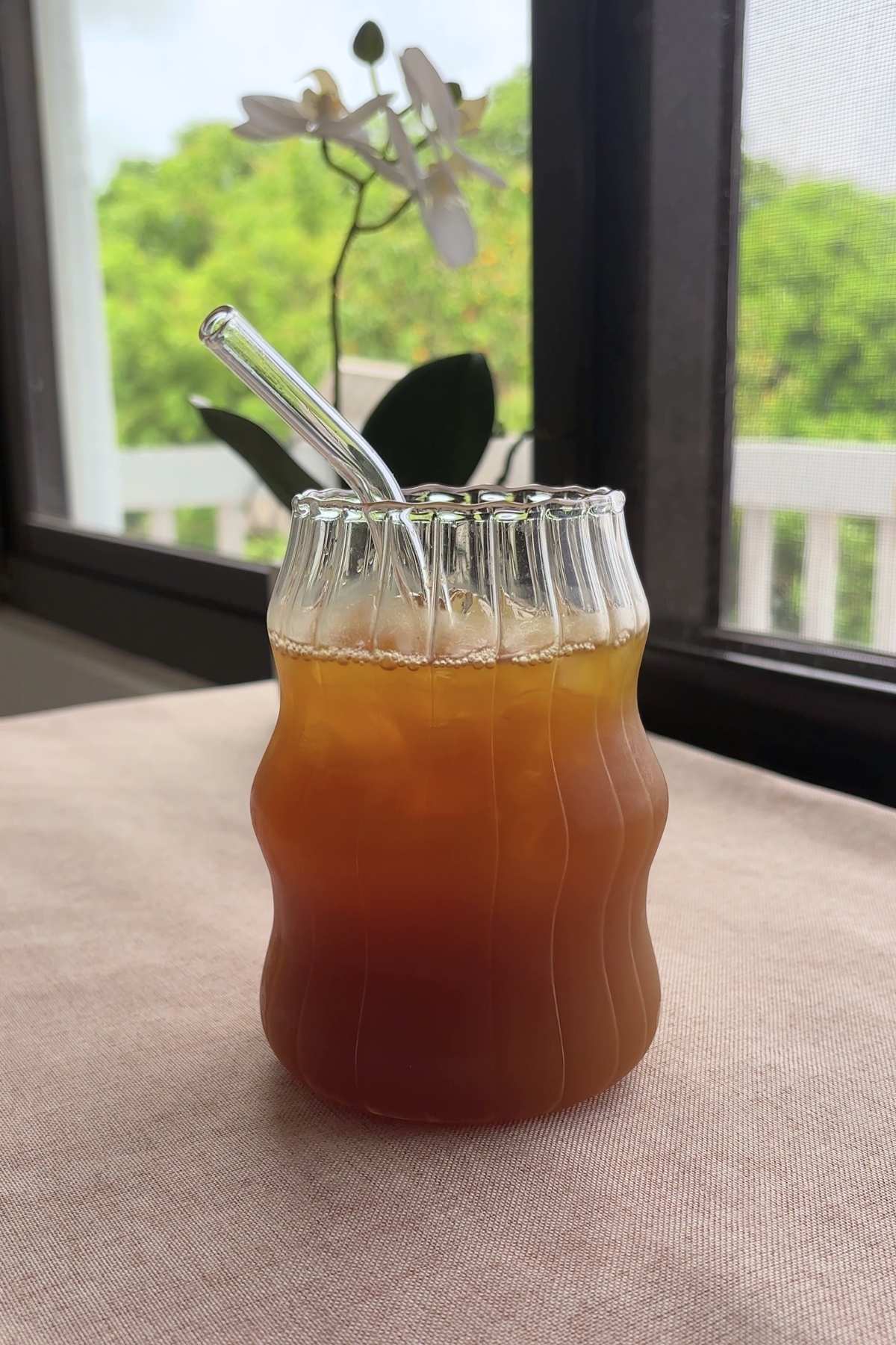 Clear straw angled down into ice-cold pineapple tea in a sculpted glass.