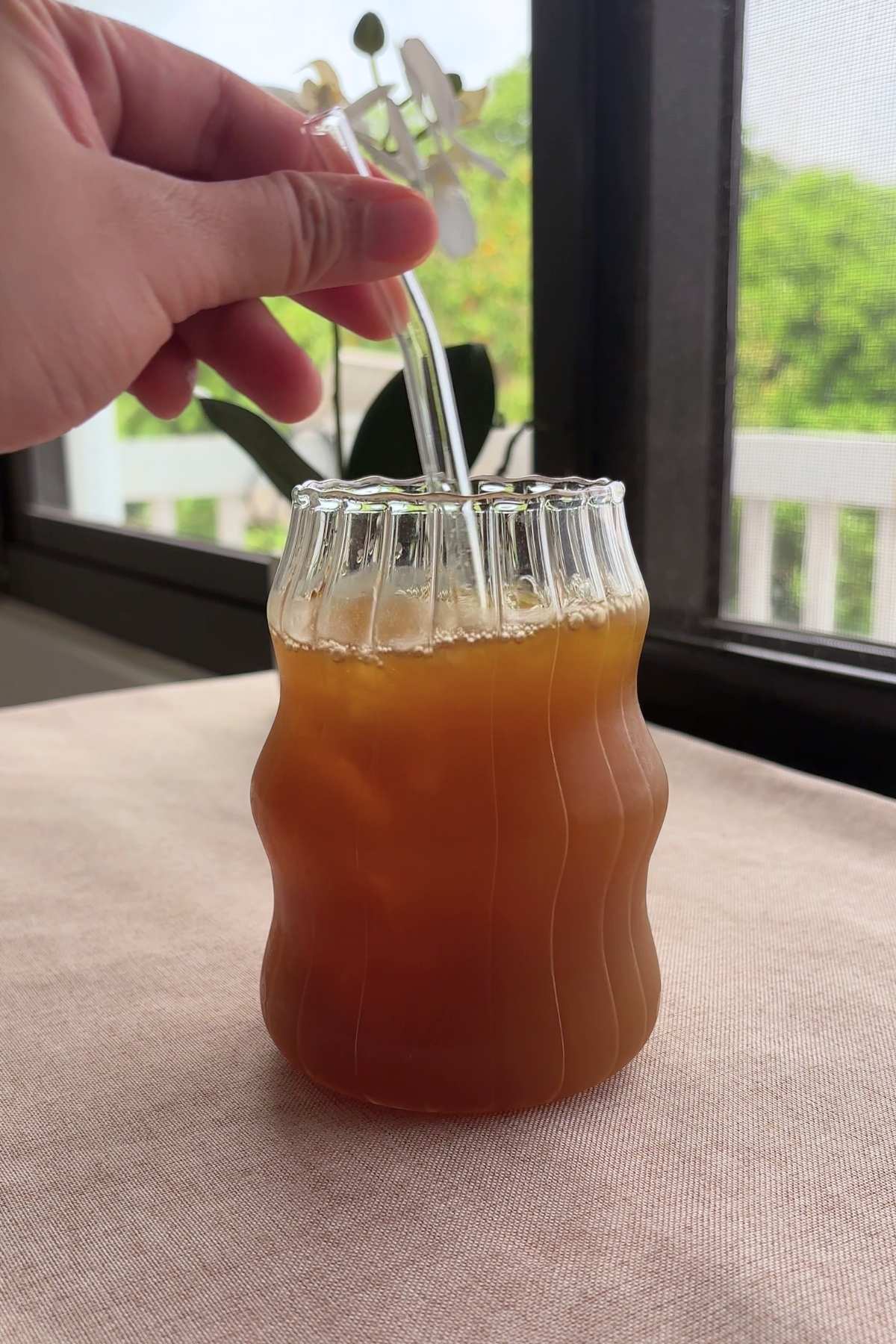 Hand holding a glass straw inside amber iced tea in a ribbed glass.