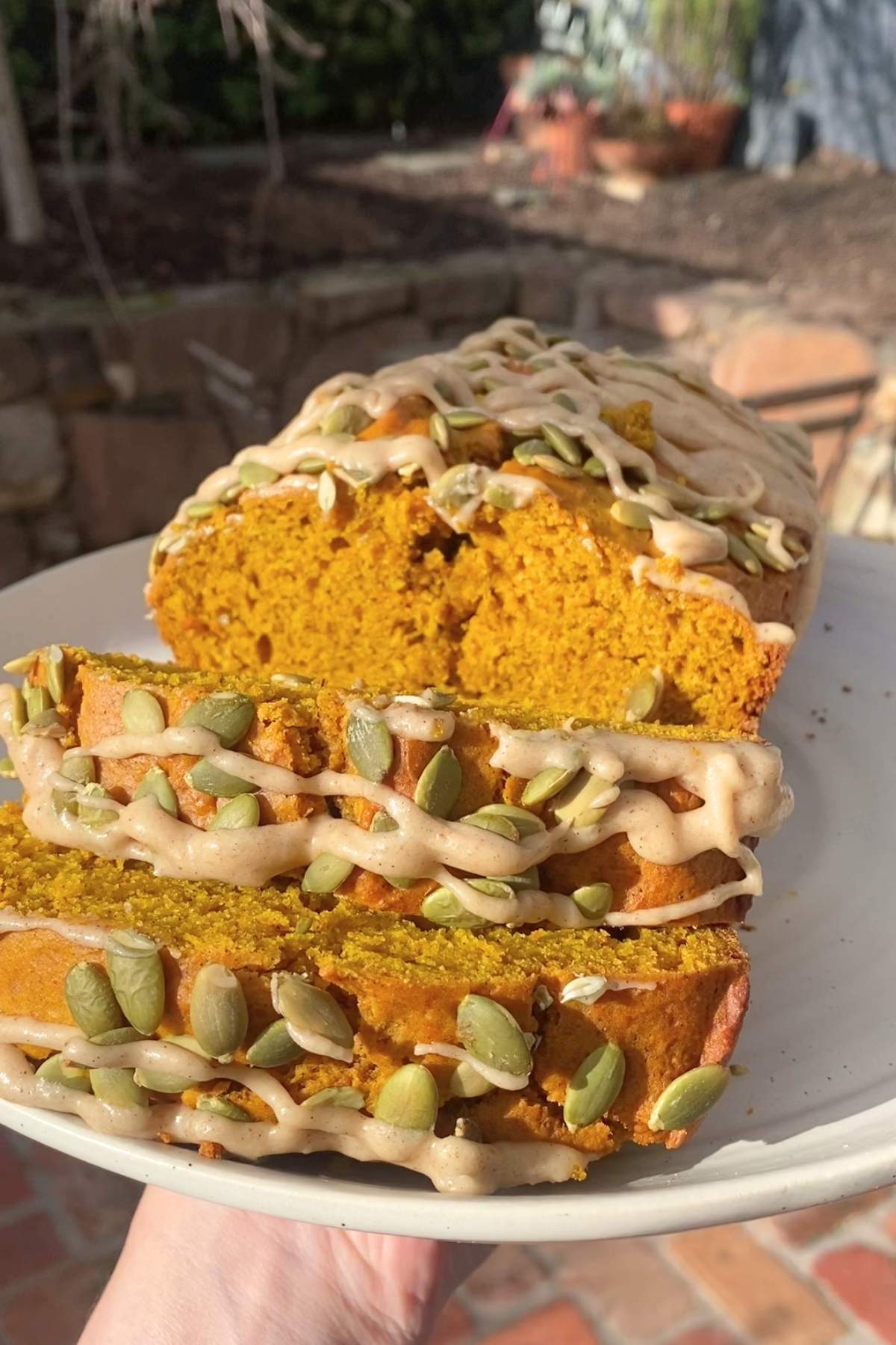 Sliced pumpkin loaf topped with ribboned maple glaze and pepitas resting on a plate.