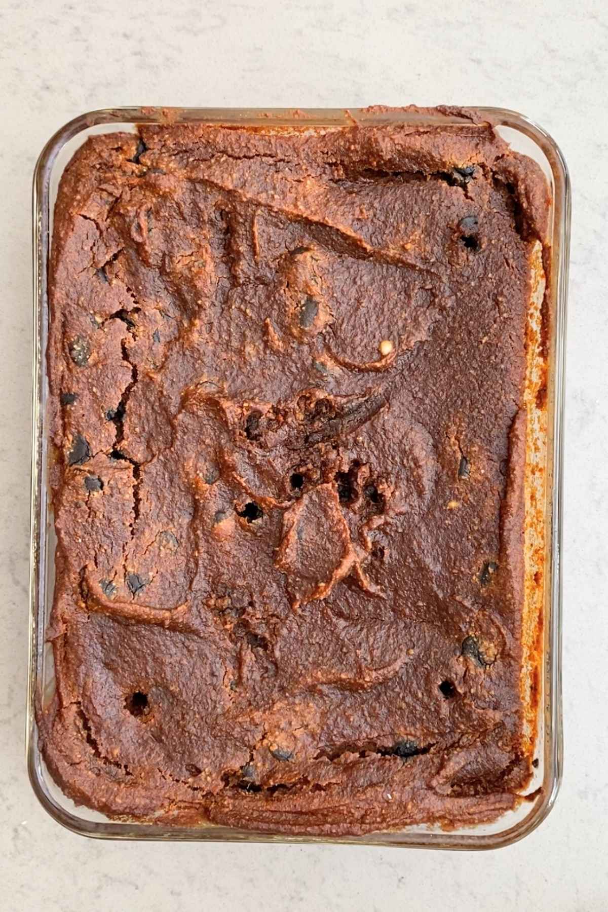 Overhead view of a full tray of baked pumpkin brownies with a textured, crackly top and dark chocolate chips throughout.