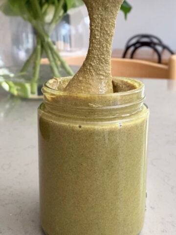 Viscous green spread drips from a spoon into a glass jar of butter.