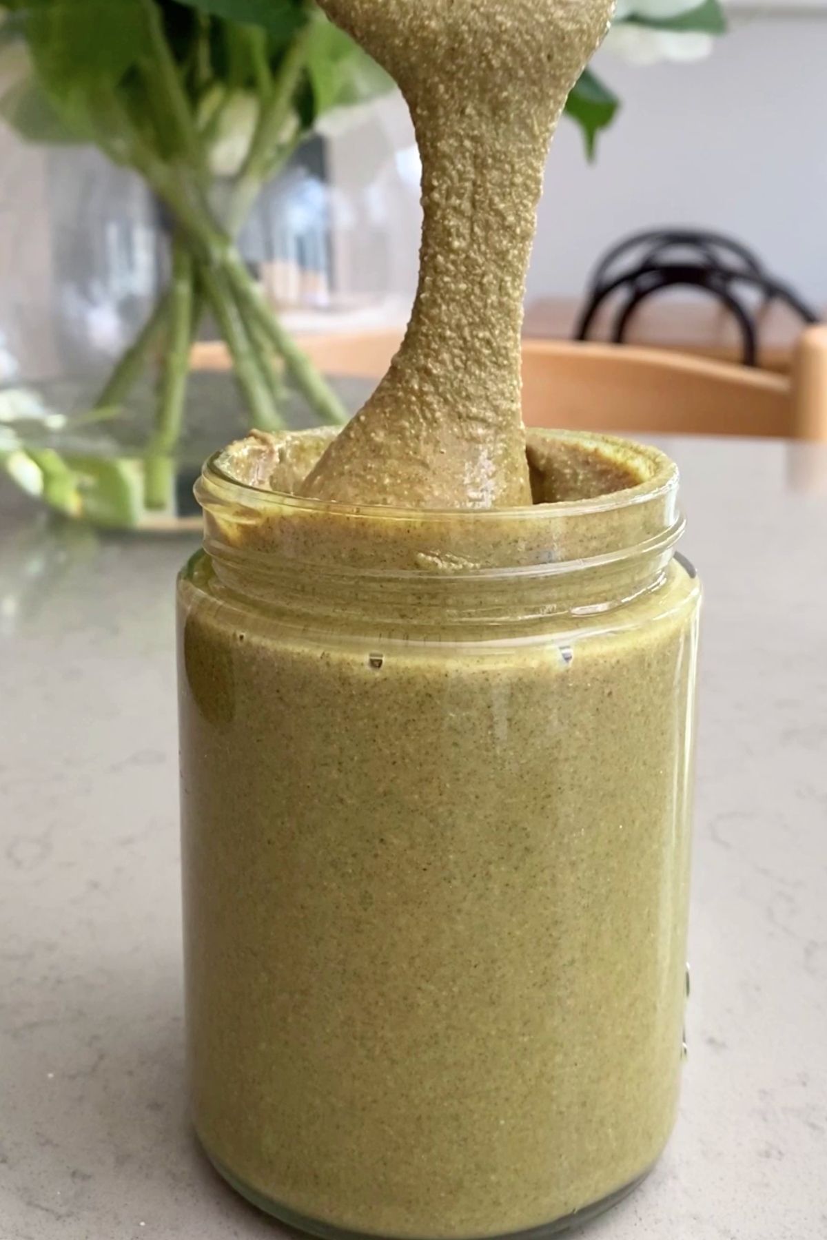 Viscous green spread drips from a spoon into a glass jar of butter.