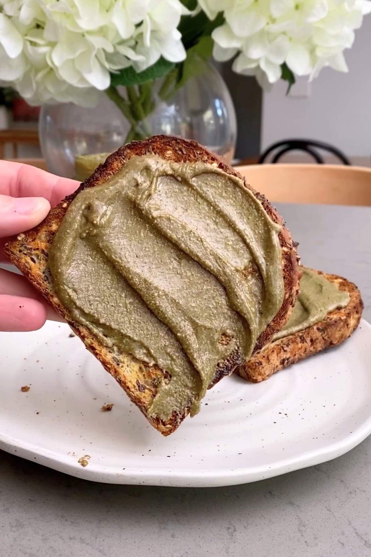 Hand holding seeded toast smeared with smooth green spread.
