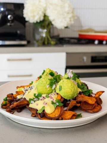 Sweet potato chips topped with creamy sauce, mashed avocado, black beans, red onion, and fresh cilantro.