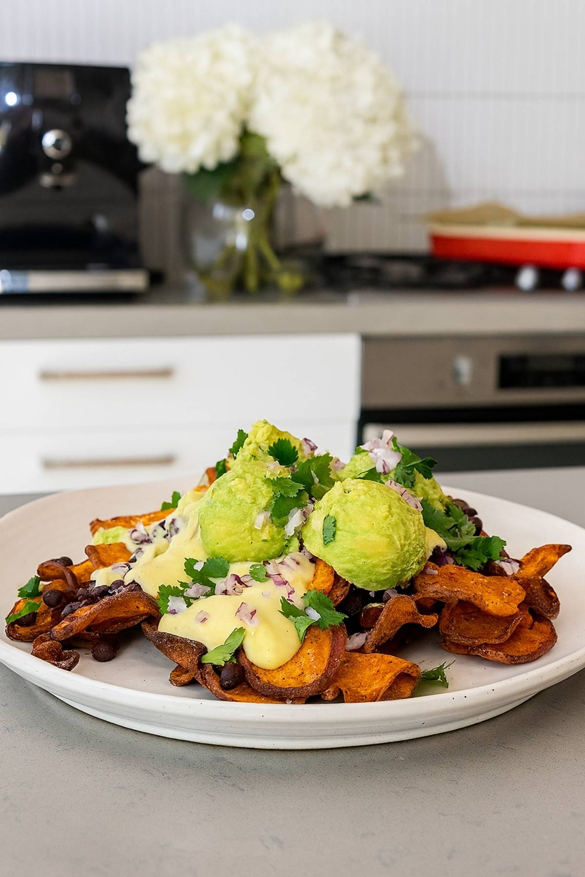 Sweet potato chips topped with creamy sauce, mashed avocado, black beans, red onion, and fresh cilantro.