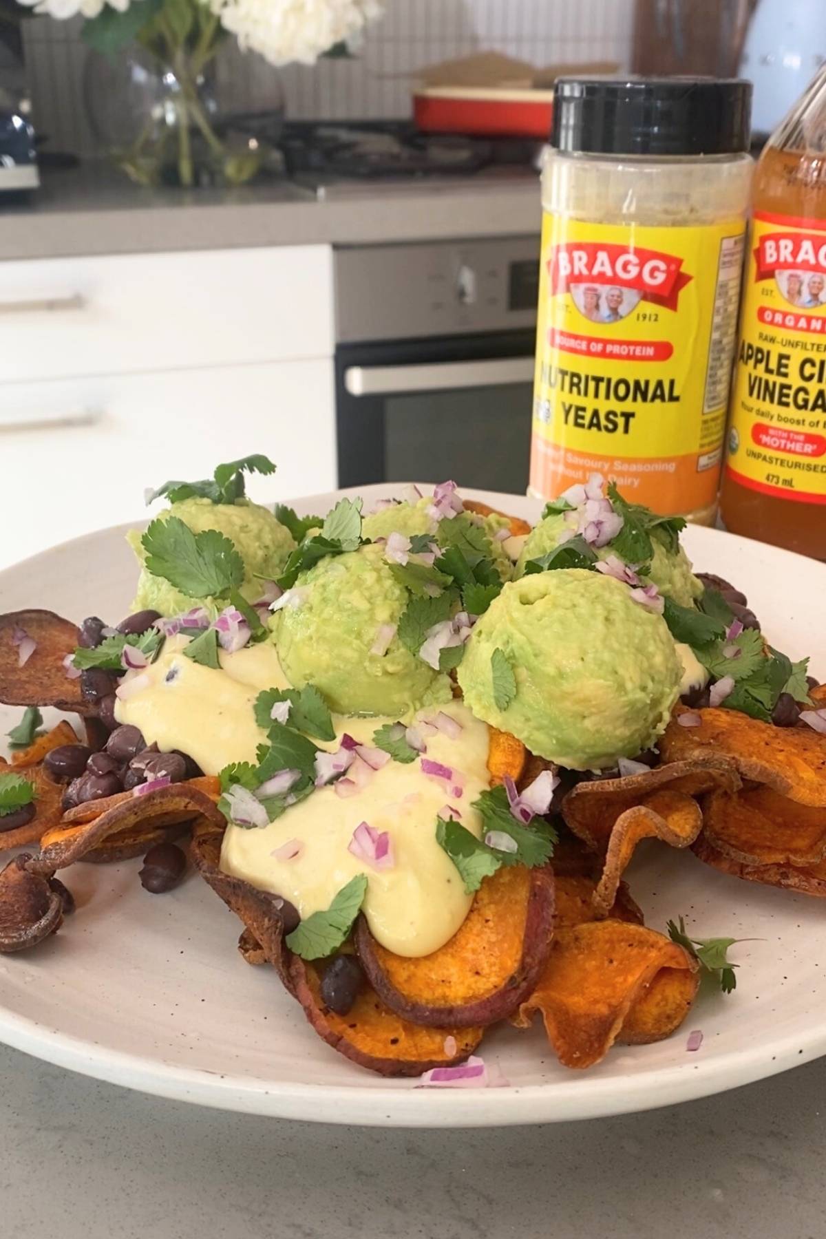 Sweet potato chips topped with creamy sauce, black beans, scoops of mashed avocado, red onion, and cilantro.