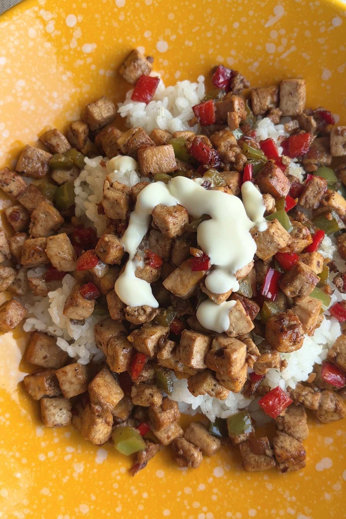 Close-up of tofu and pepper mixture over rice with a thick vegan mayo drizzle.