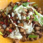 Crispy tofu cubes and diced peppers piled on white rice in a yellow bowl, drizzled with creamy mayo and scattered green onion slices.