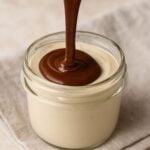 Smooth chocolate ganache being poured over creamy cashew mousse in a glass jar.