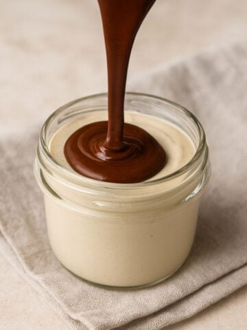 Smooth chocolate ganache being poured over creamy cashew mousse in a glass jar.