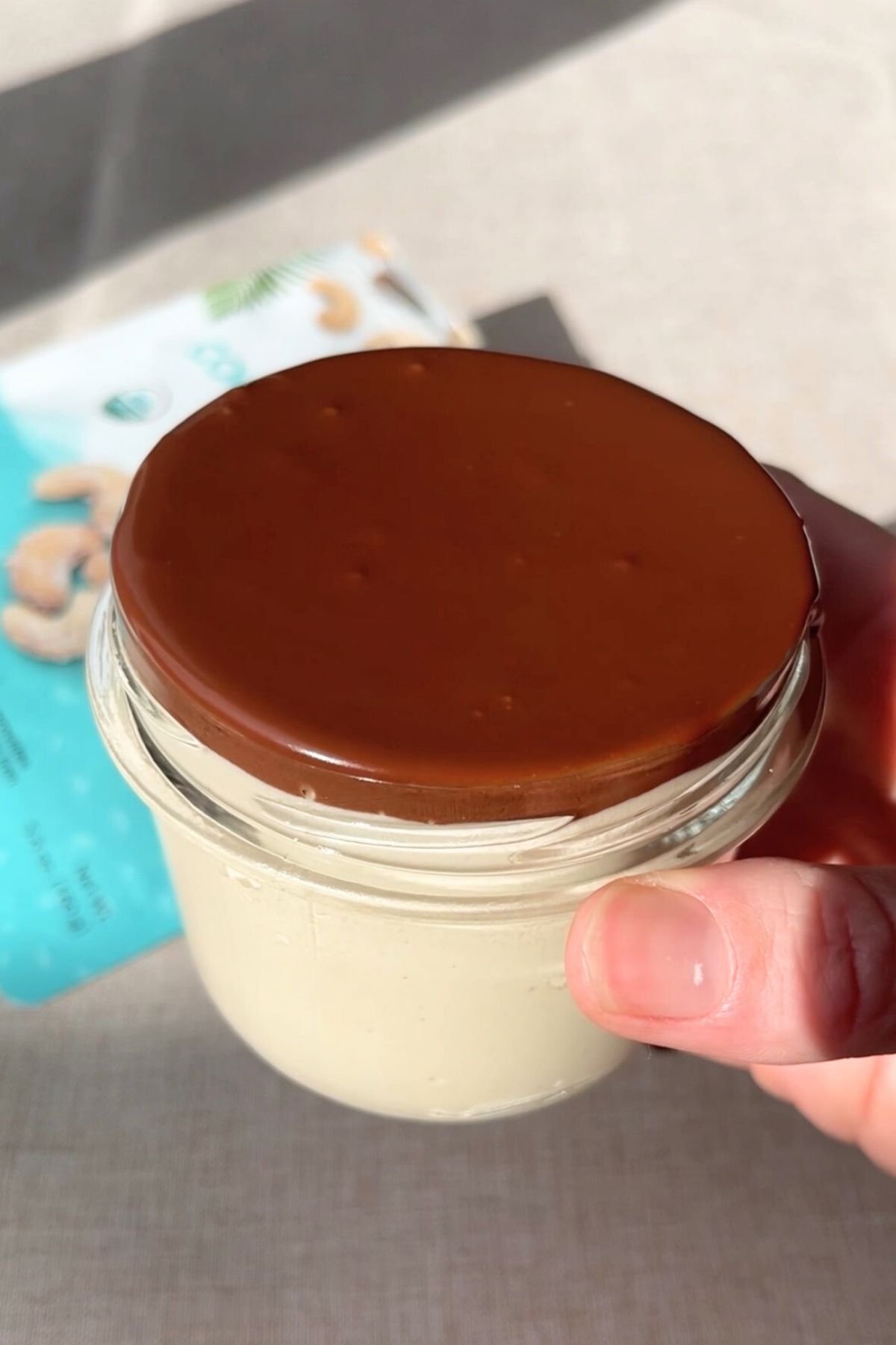 Thick chocolate ganache being poured over a jar of mousse.