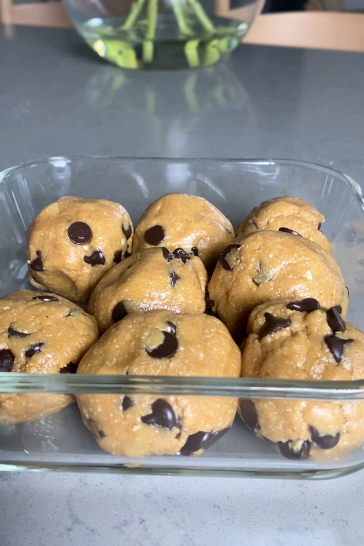 Glass container filled with several dough balls studded with chocolate chips.