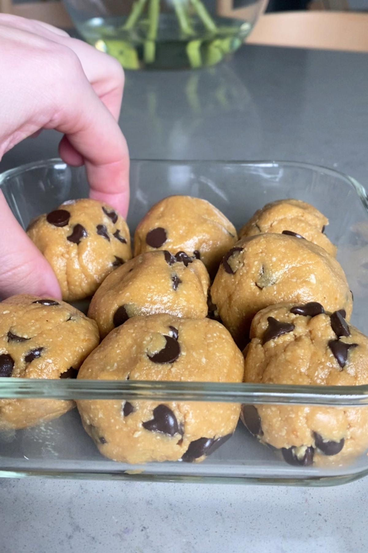 Hand placing a dough ball into a glass container filled with similar balls.