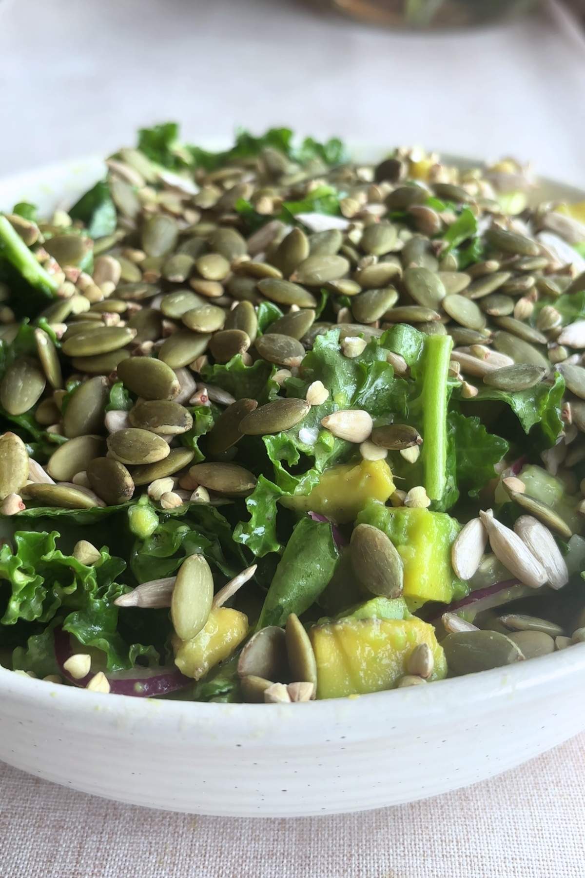 Bowl of kale salad topped with pumpkin and sunflower seeds.
