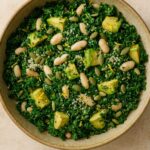 Fresh kale salad with avocado chunks, white beans, and seeds in a neutral ceramic bowl.