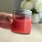Hand holding a small jar of pink guava jam with a silver lid.