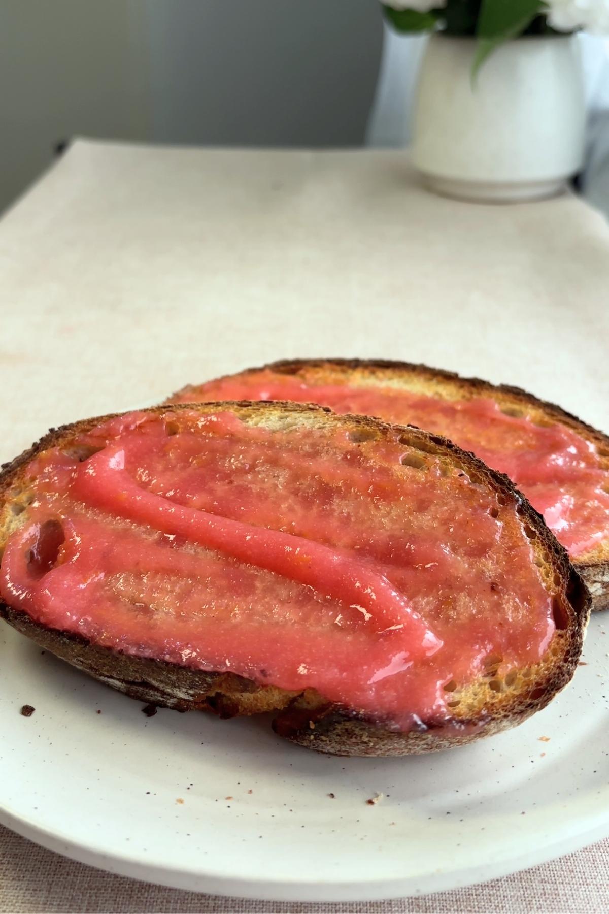 Slices of toasted bread spread with glossy pink guava jam, held in hand.