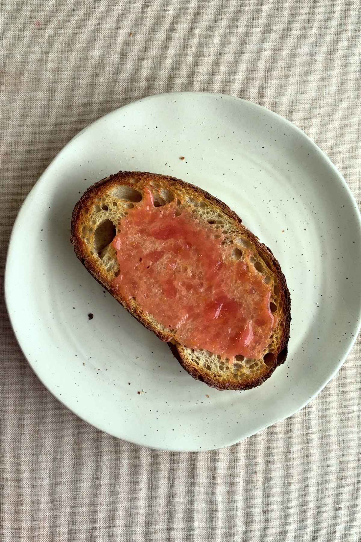 Single slice of toast spread with pink guava jam on a white plate.