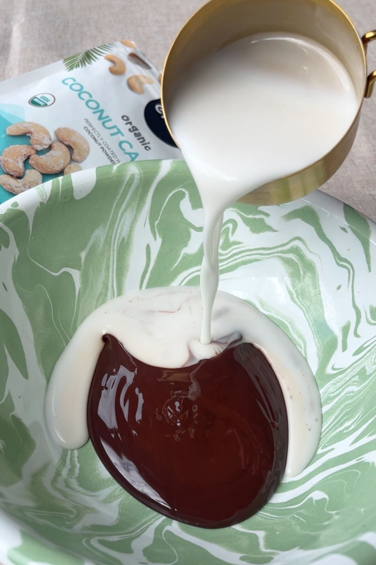 Coconut milk being poured into a bowl of melted chocolate.