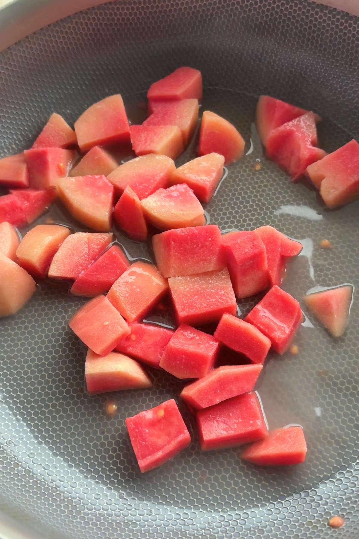 Diced pink guava pieces simmering in liquid in a saucepan.