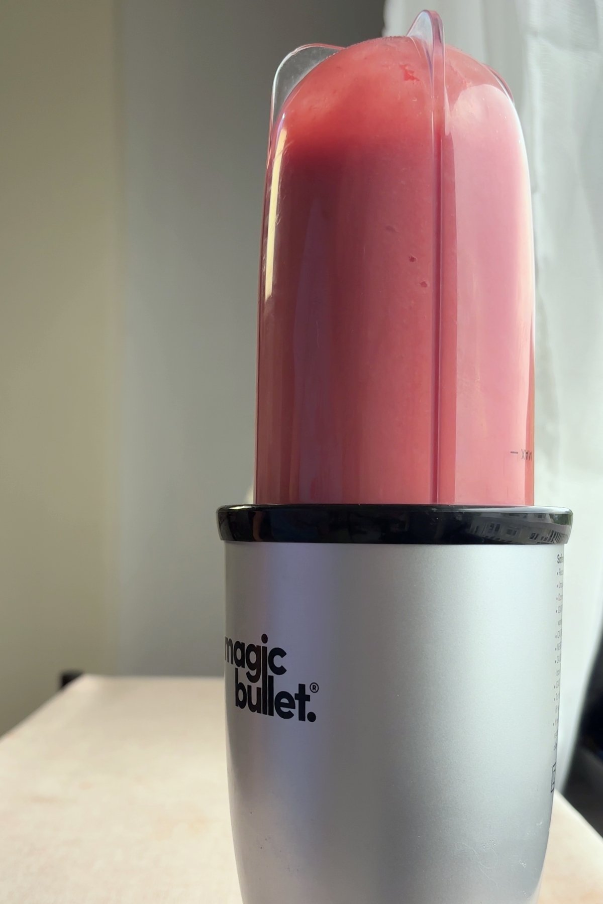 Tall blender cup filled with pink guava puree attached to a Magic Bullet base.