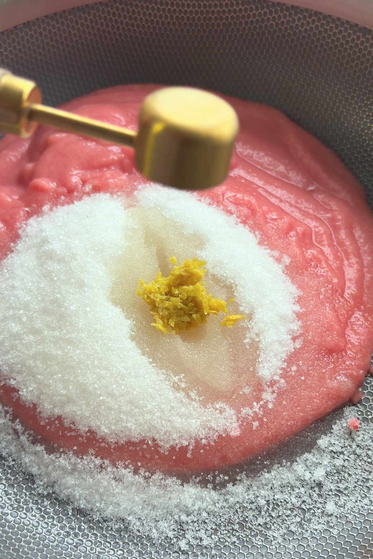 Pink guava puree topped with white sugar and fresh lemon zest in a saucepan.