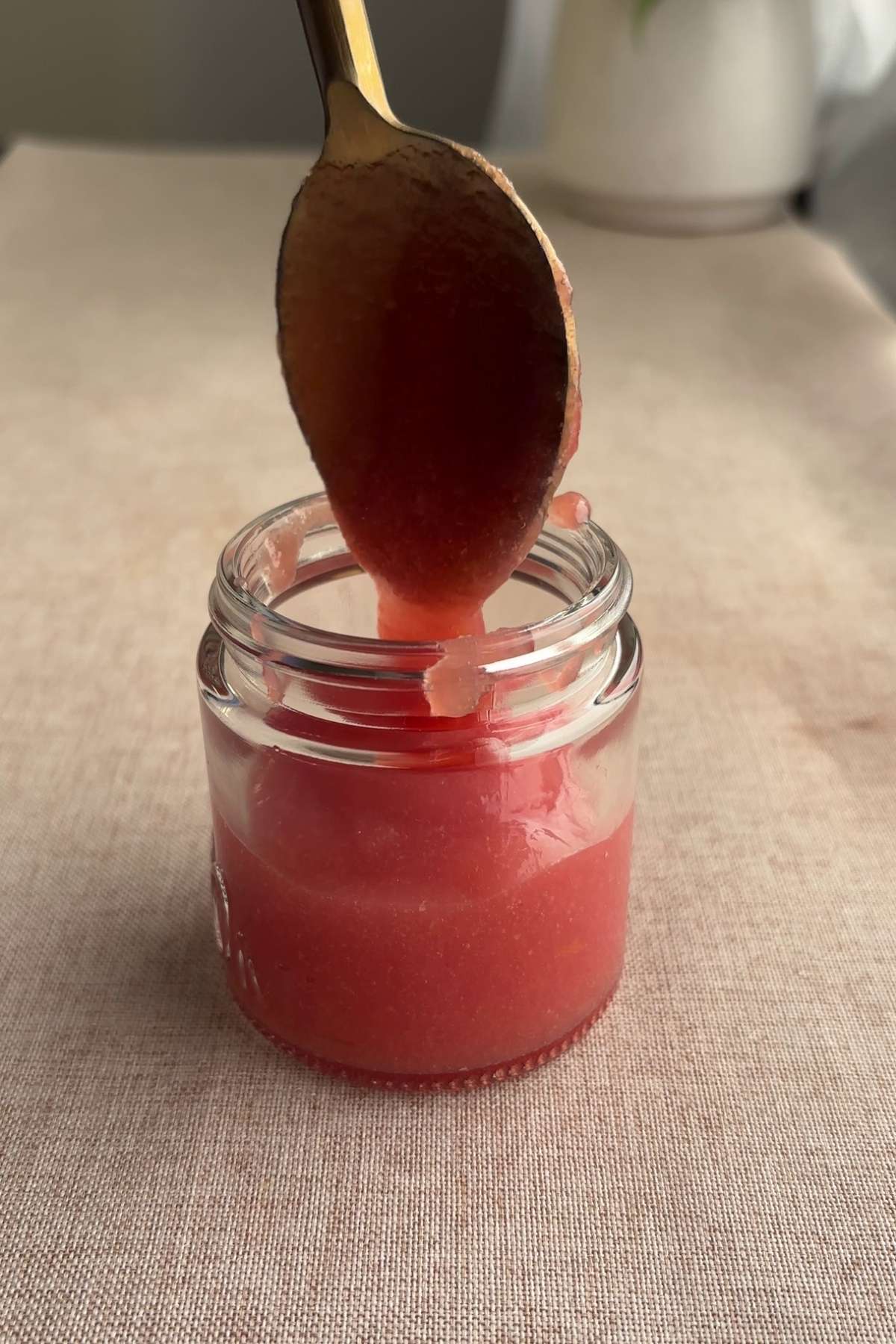 Spoon putting pink guava jam into a small glass jar.