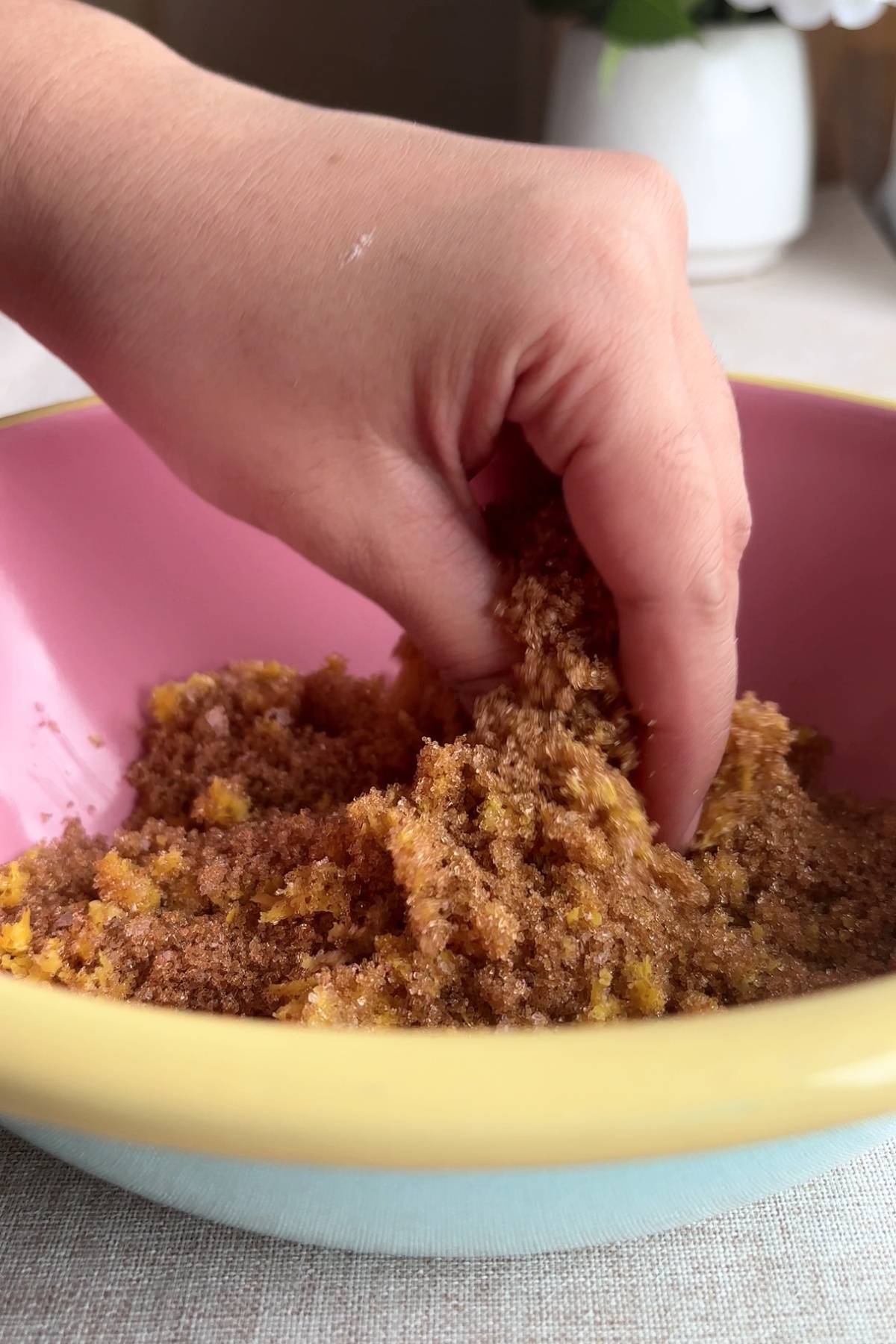 Hand mixing sugar and lemon zest in a pink bowl.