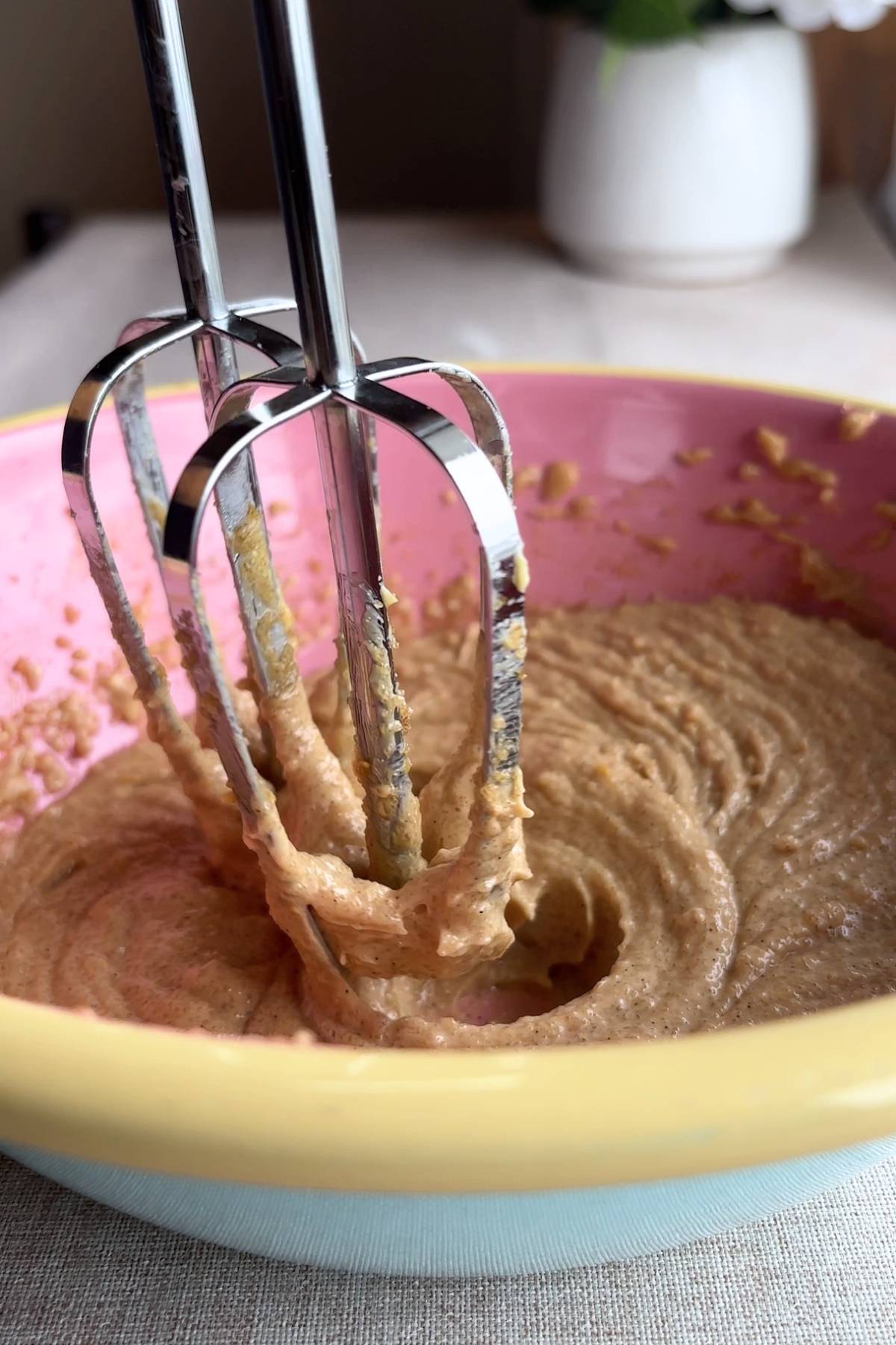 Electric beaters blending a creamy mixture in a pink bowl.