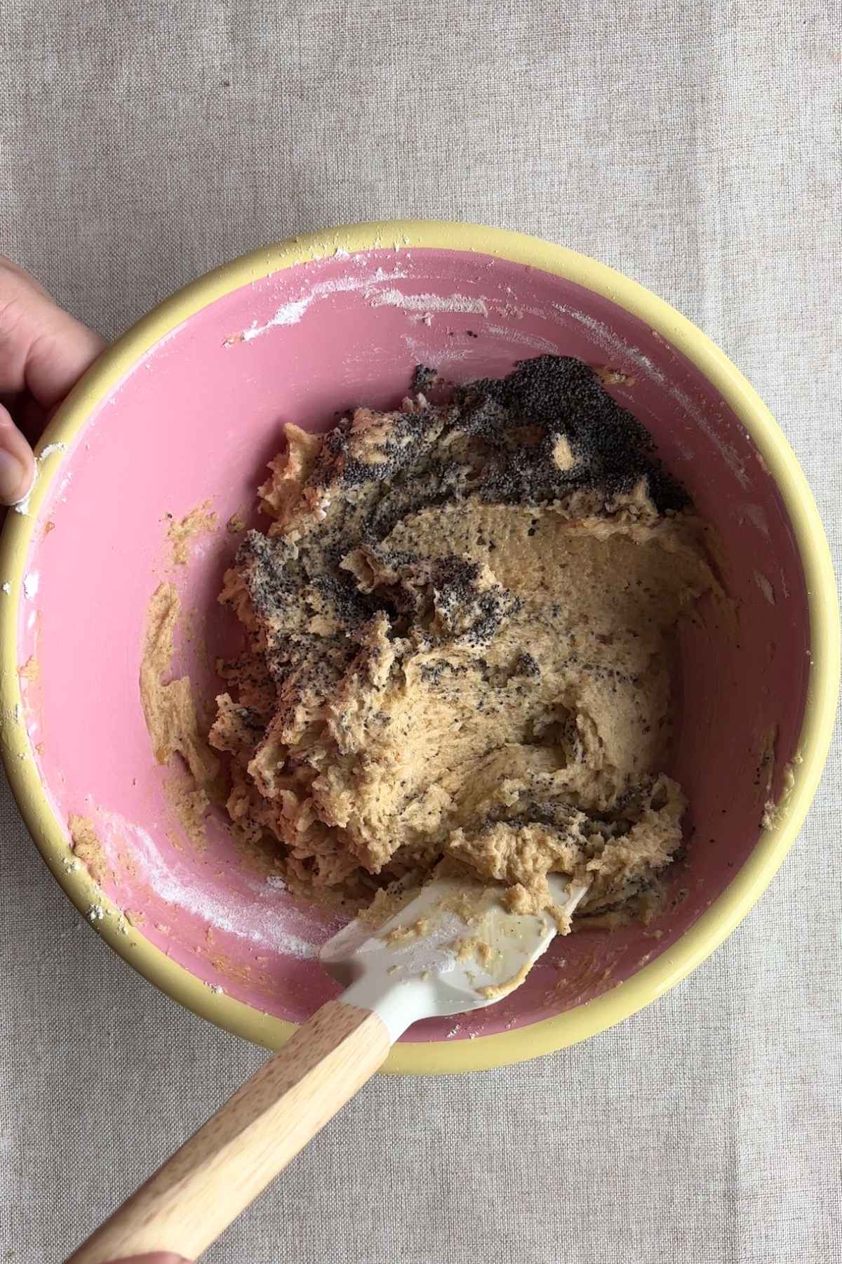 Cookie dough with poppy seeds being mixed in a bowl.