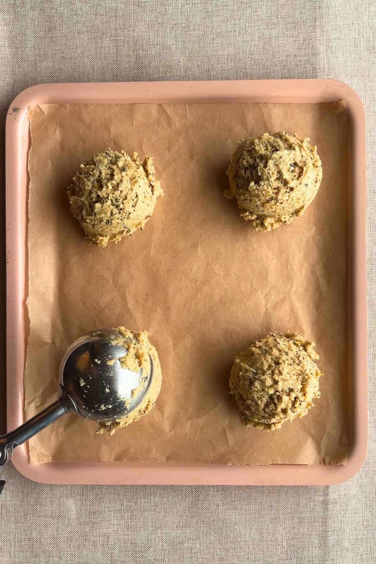 Four scoops of cookie dough on a lined baking tray.