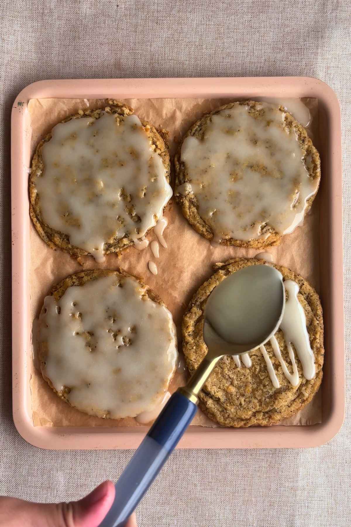 Spoon drizzling glaze over cookies on a tray.