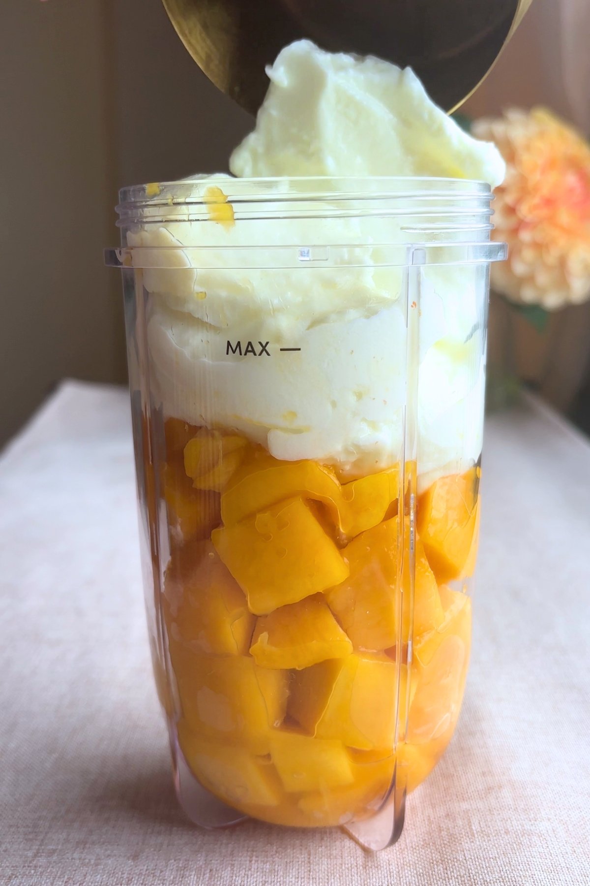 Chopped mango and yogurt layered in a blender cup, filled close to the max line.