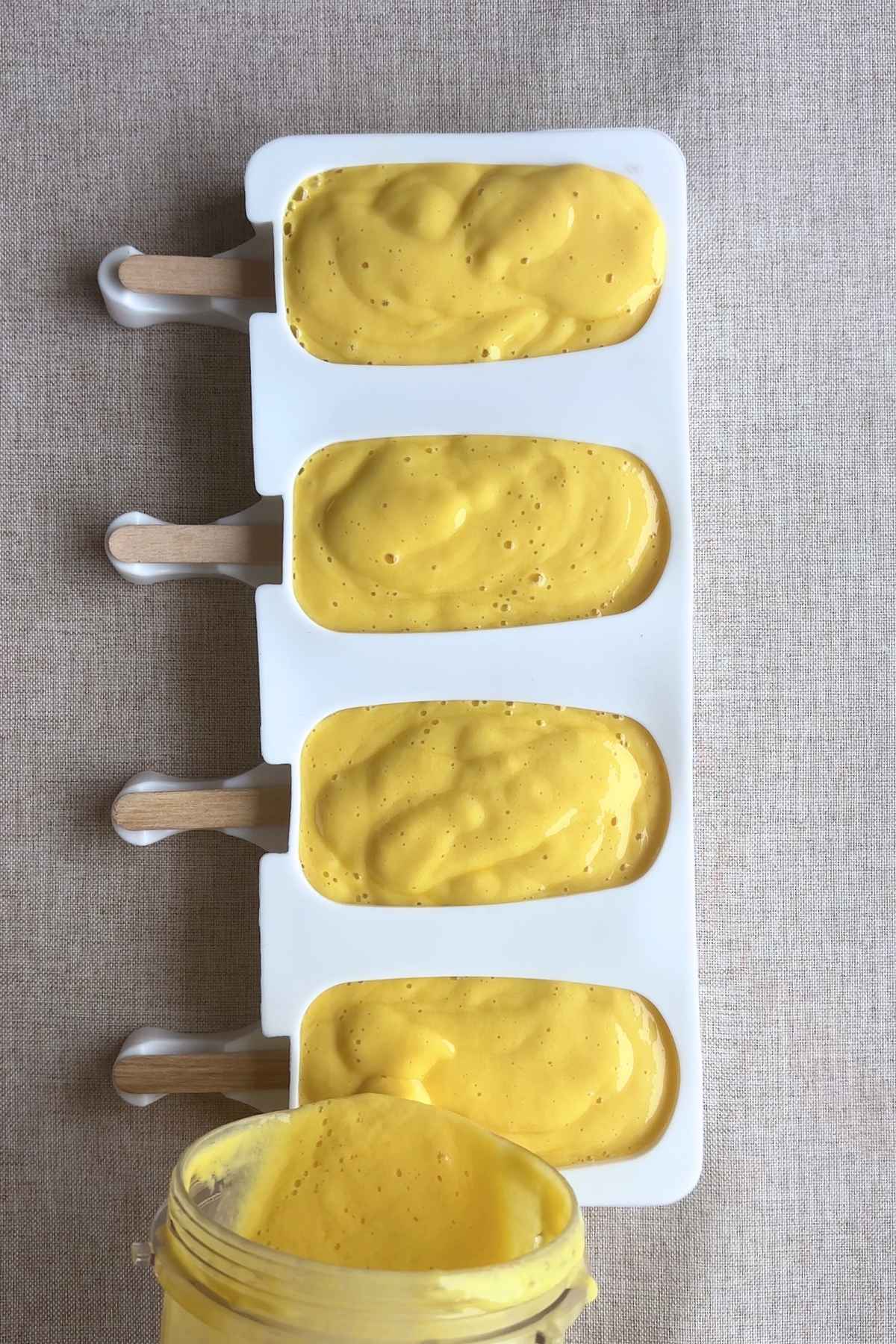 Freshly blended mango mixture poured into popsicle molds with wooden sticks.