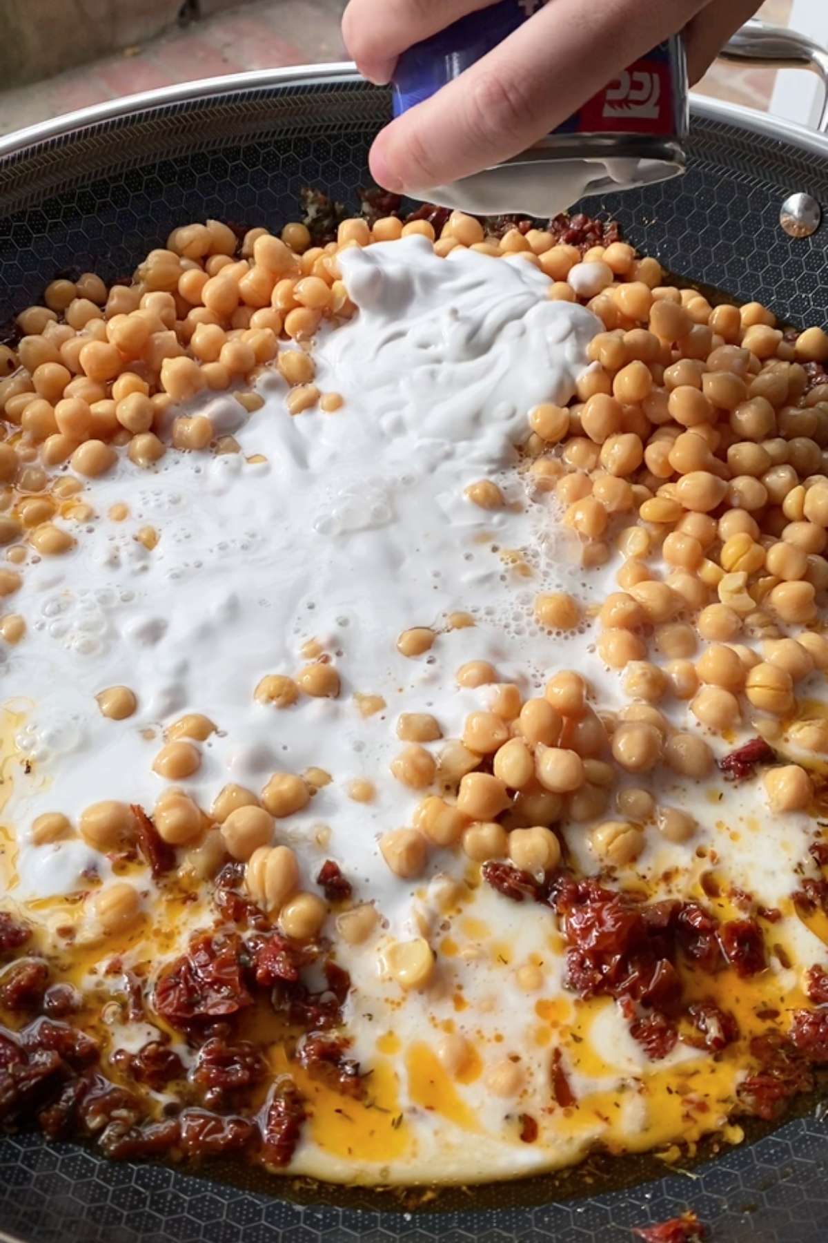 Chickpeas and coconut milk being poured into the skillet.