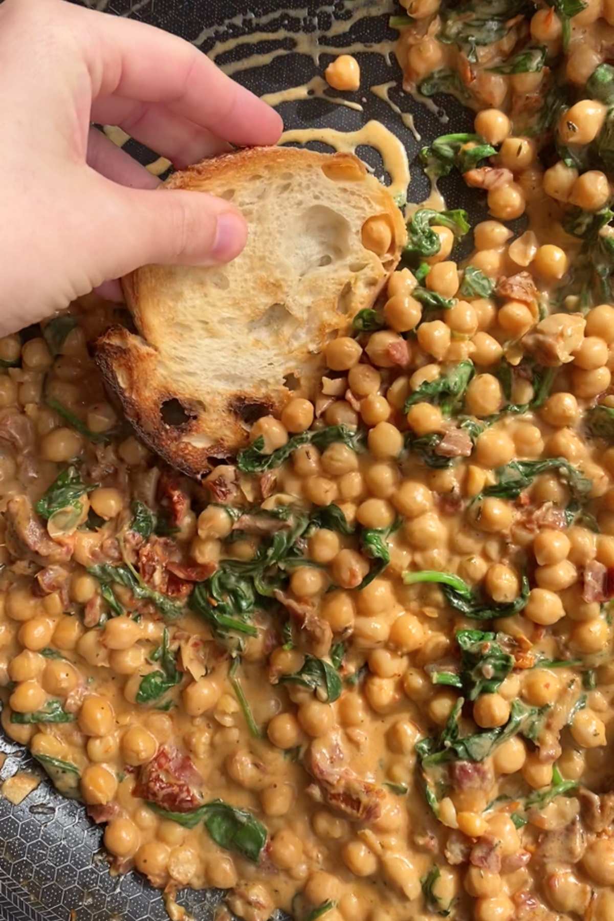 Hand dipping toasted bread into creamy chickpeas with spinach.