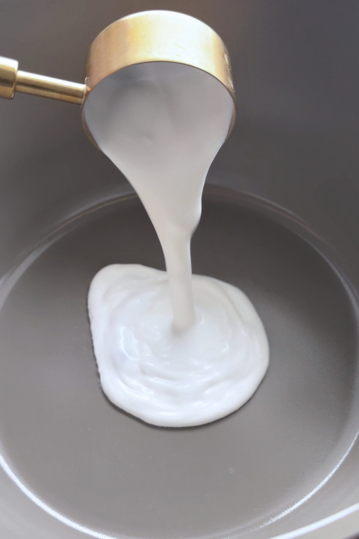 Thick coconut cream being poured into a pot.