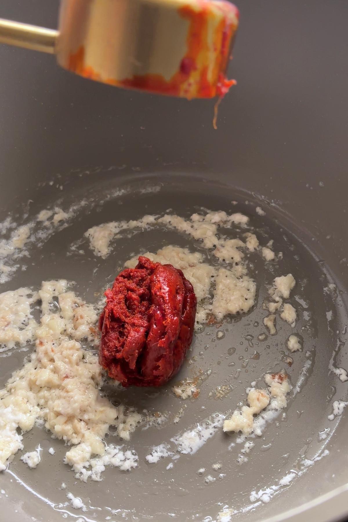 Red curry paste added to sautรฉed garlic and ginger in a pot.