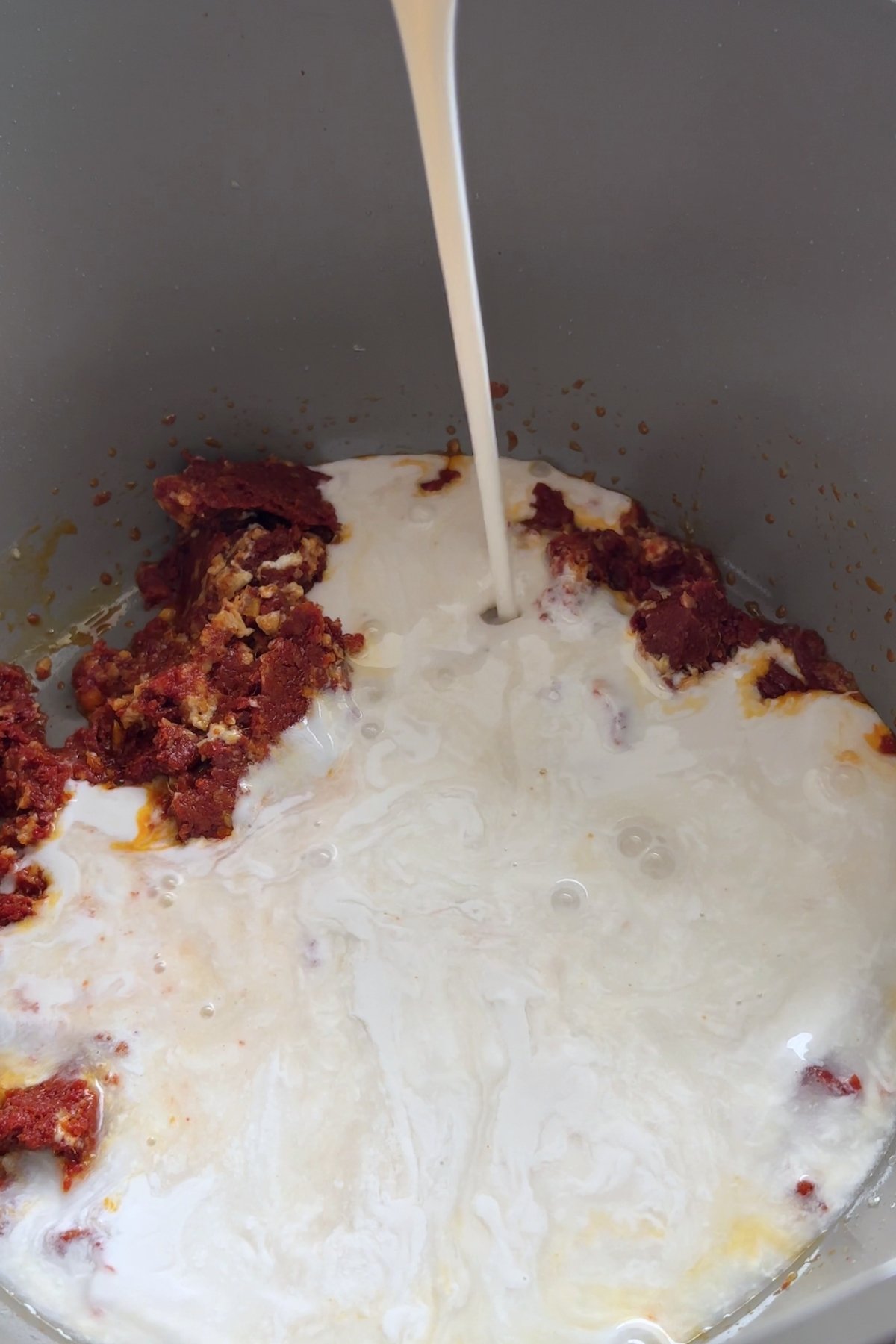 Coconut milk being poured into a pot with curry paste.