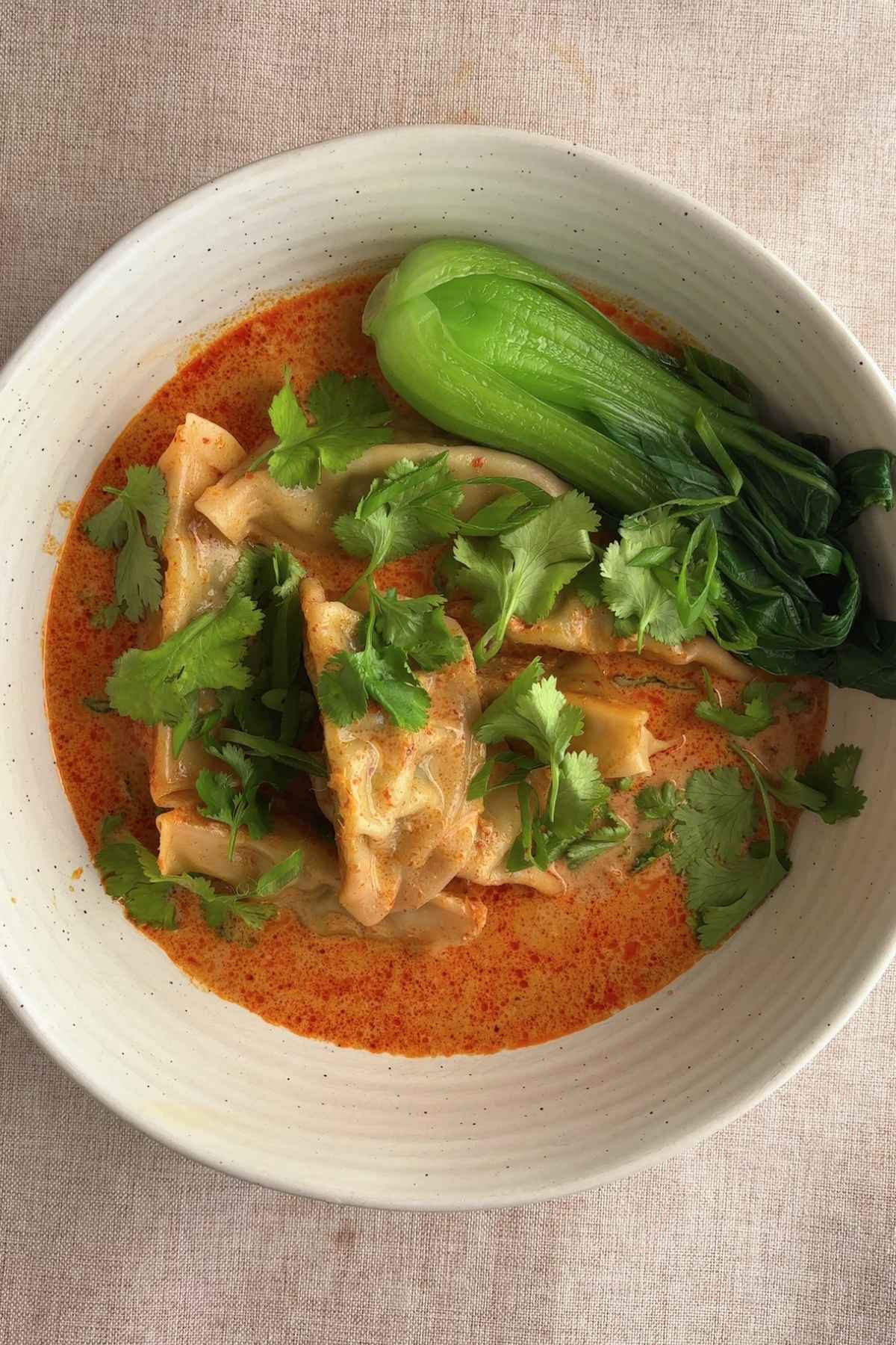 Bowl of dumpling soup with bok choy and cilantro garnish.