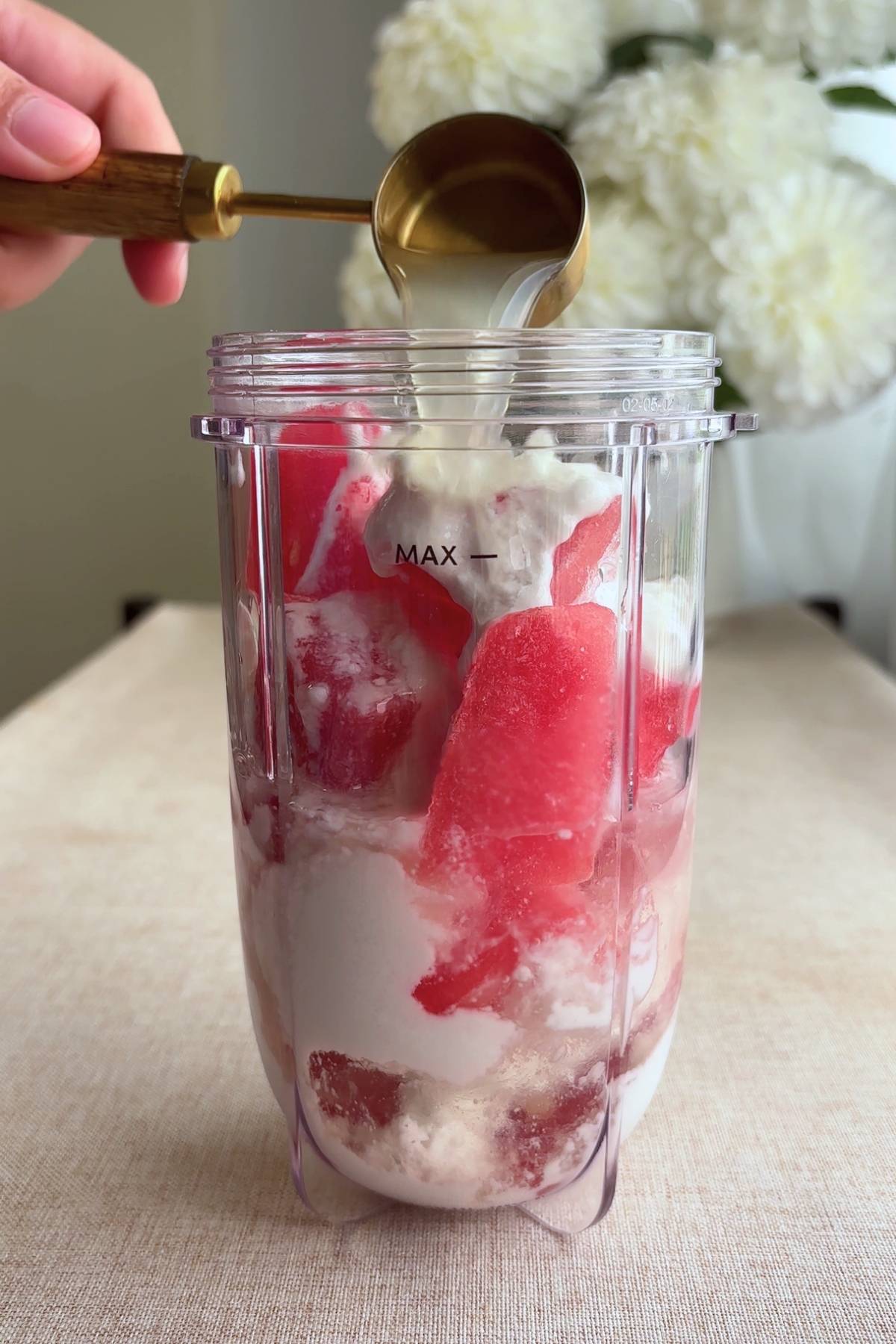 Pouring lime juice into a blender cup with frozen watermelon and coconut cream.