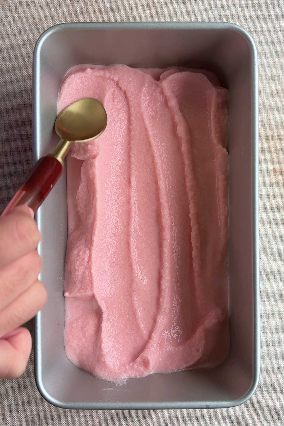 Smoothing sorbet into a loaf pan with a gold spoon.