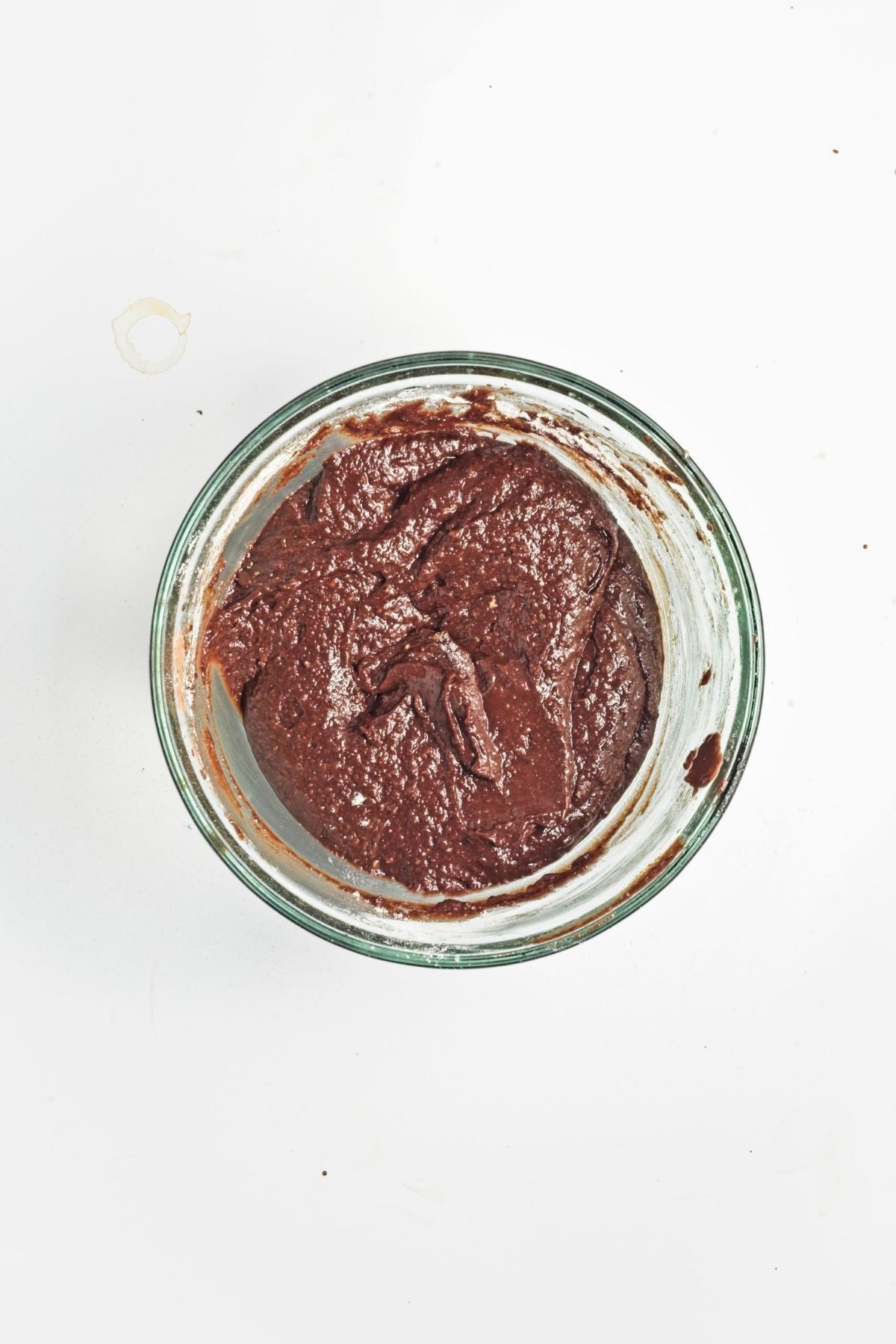 Thick chocolate brownie batter in a glass bowl.