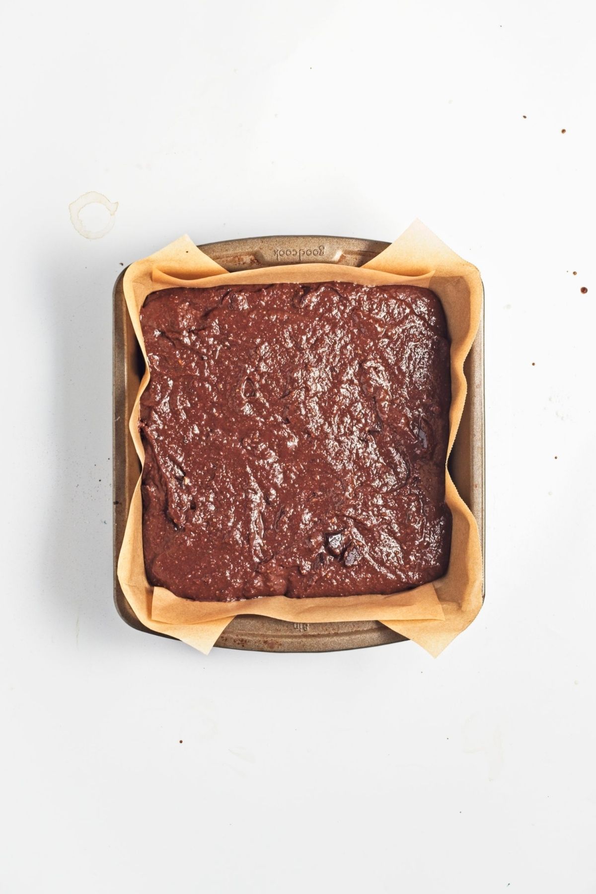Unbaked brownie batter spread in a parchment-lined square pan.