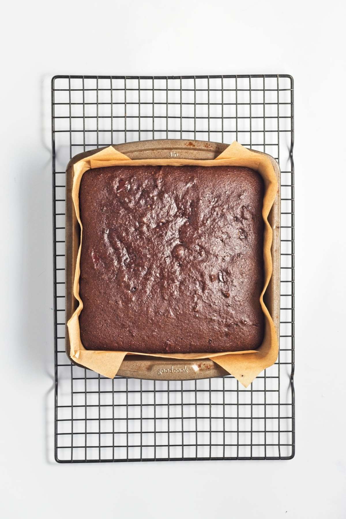 Baked brownie slab cooling in a parchment-lined pan on a wire rack.