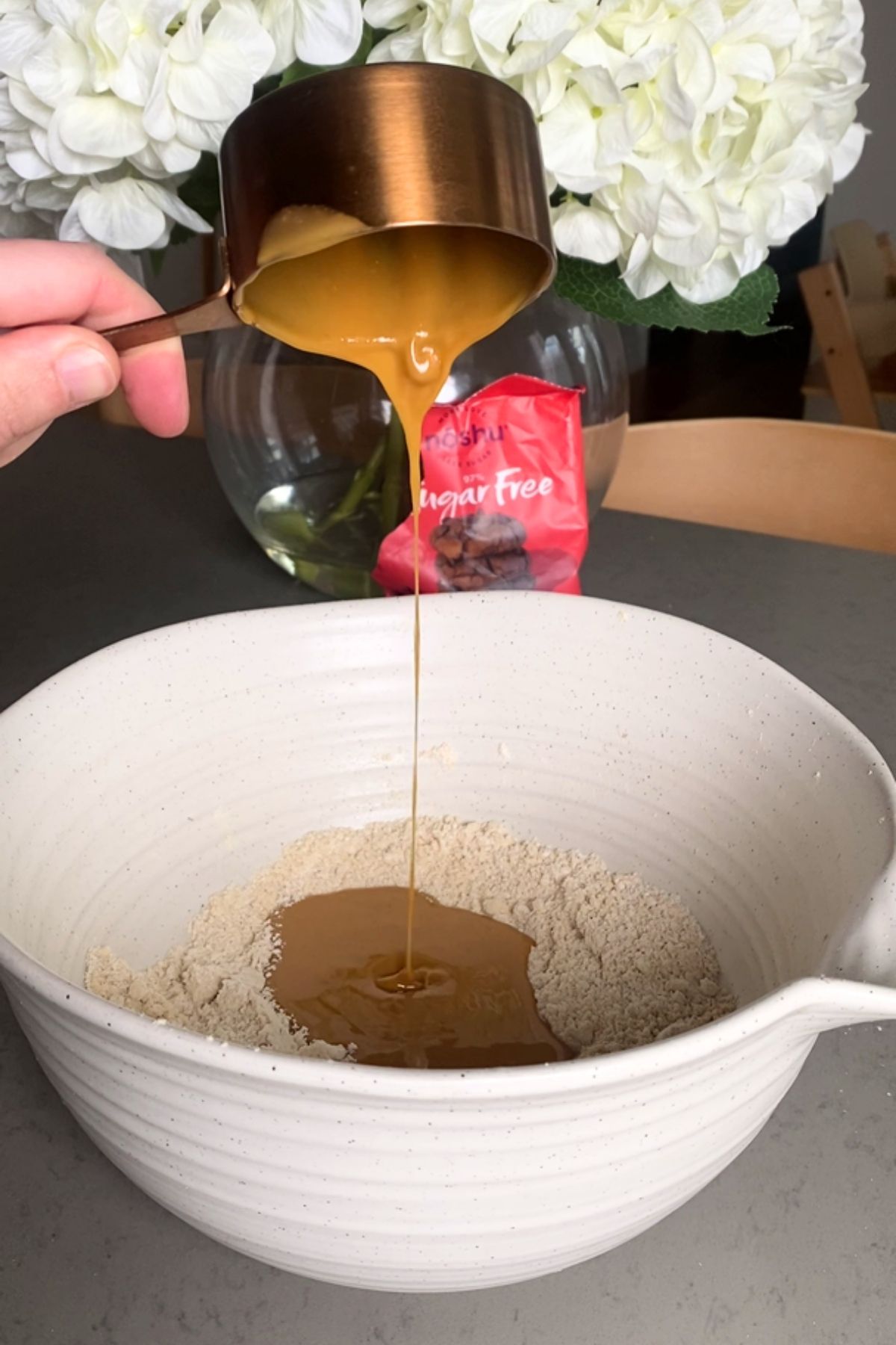 Peanut Butter being poured from a measuring cup into a mixing bowl with oat flour.