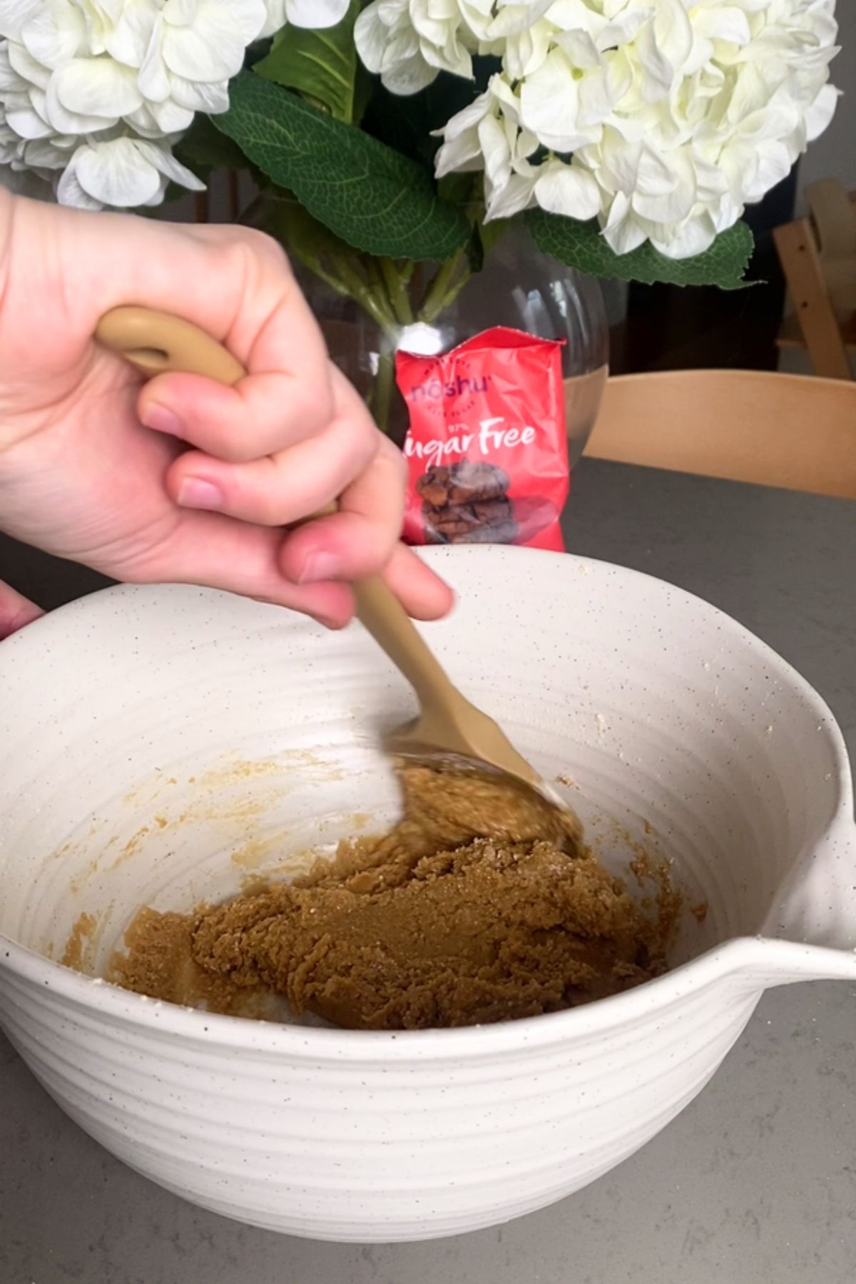 Hand stirring a mixture in a white bowl with a spatula.