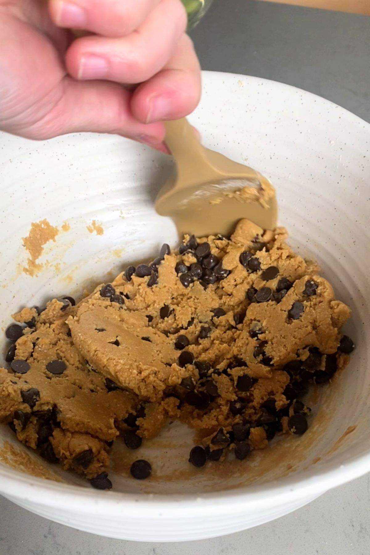 Mixing chocolate chips into a thick dough in a white bowl.