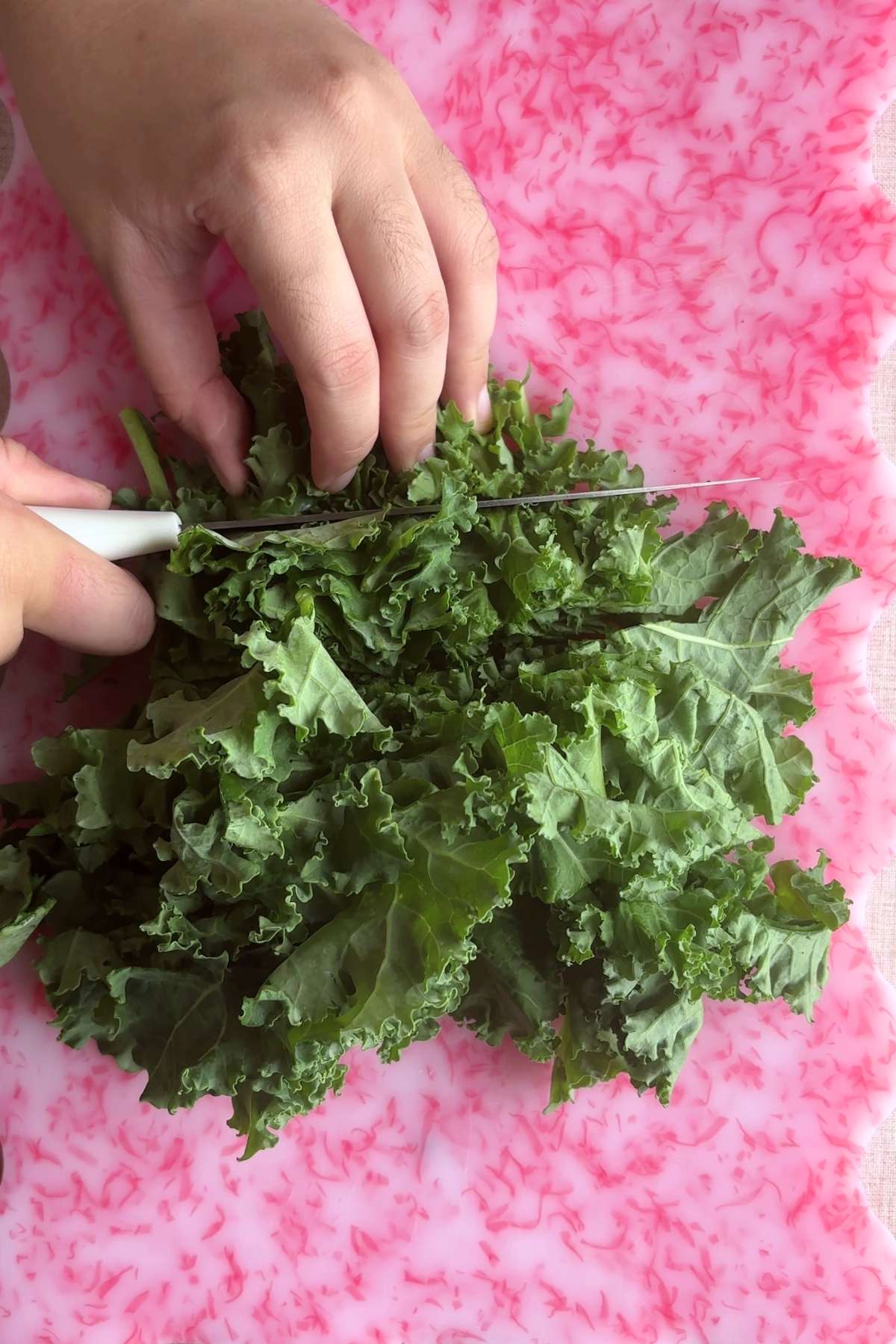 Hand chopping fresh kale on a cutting board.